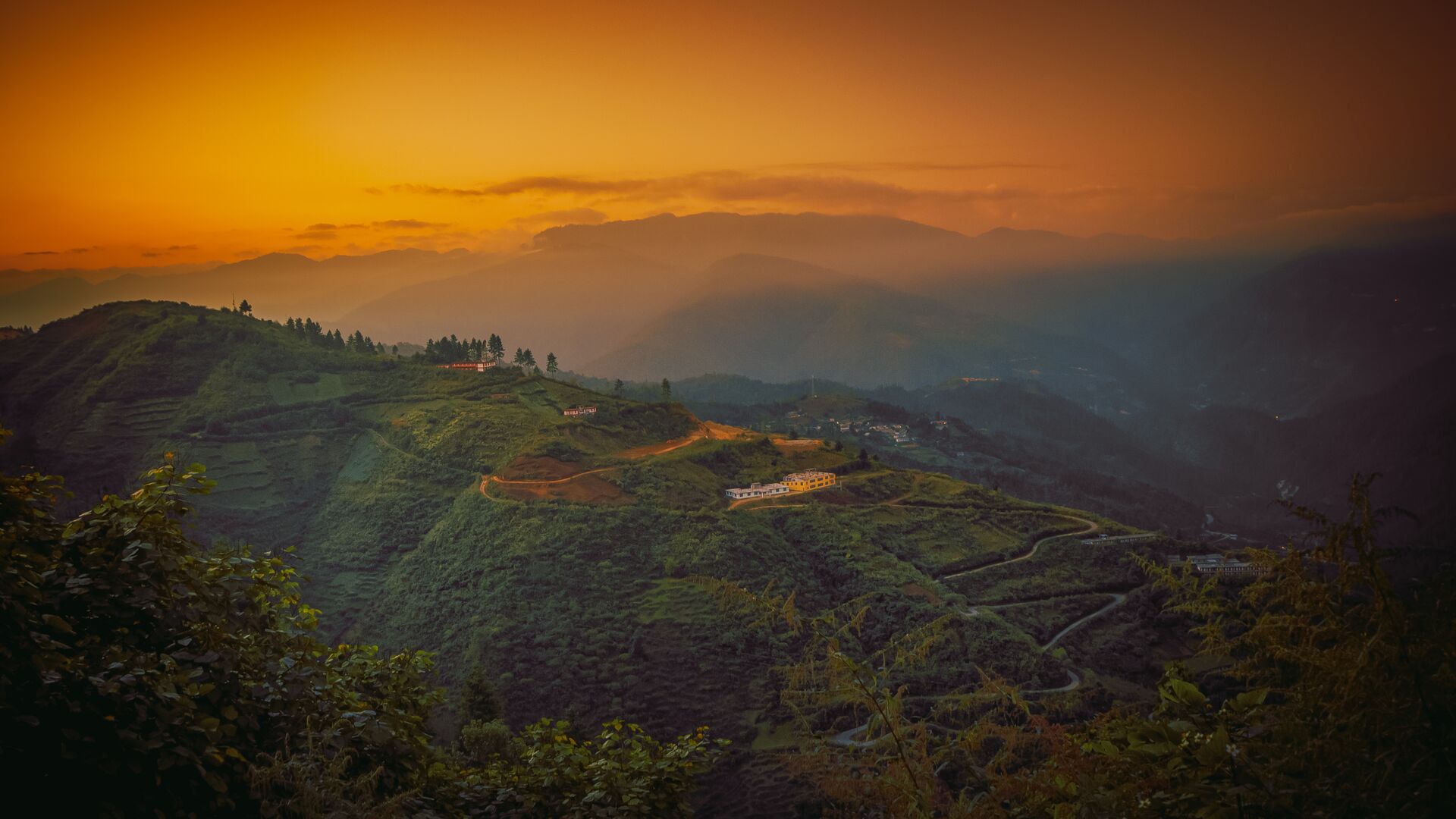 A view over Dirang Valley in Arunachal Pradesh, India, as the sun rises over buildings on a hilltop.