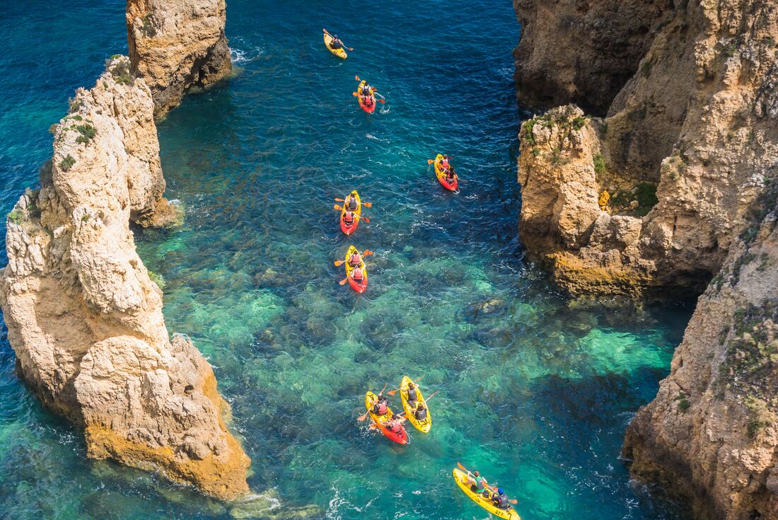 Aerial view of string of travellers in double kayaks between pale protruding cliffs near Lagos in Portugal