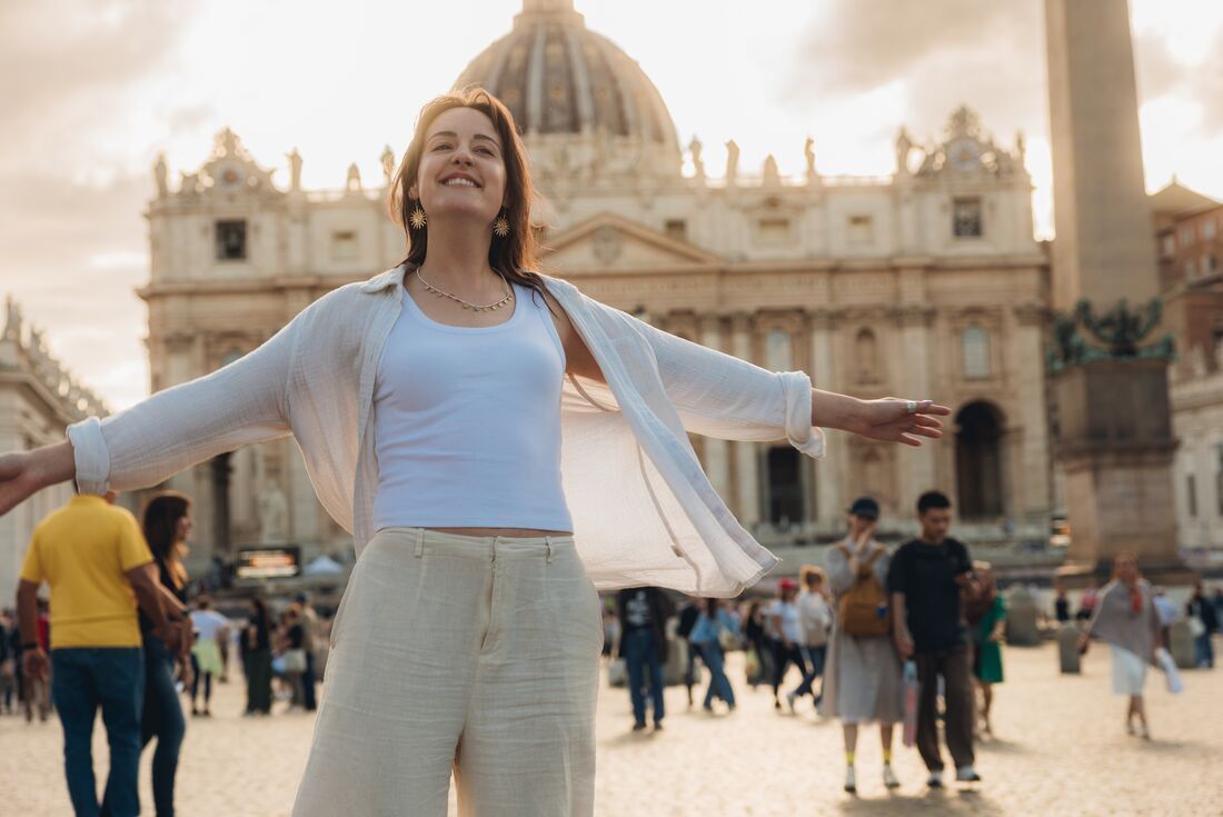 Smiling traveller posing in St. Peter's Square with  St. Peter's Basilica in the background during sunset, Vatican Square, Italy