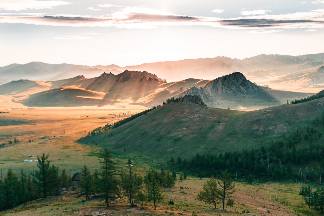 Early light streams through clouds over rolling hills in Terelj National Park, Mongolia