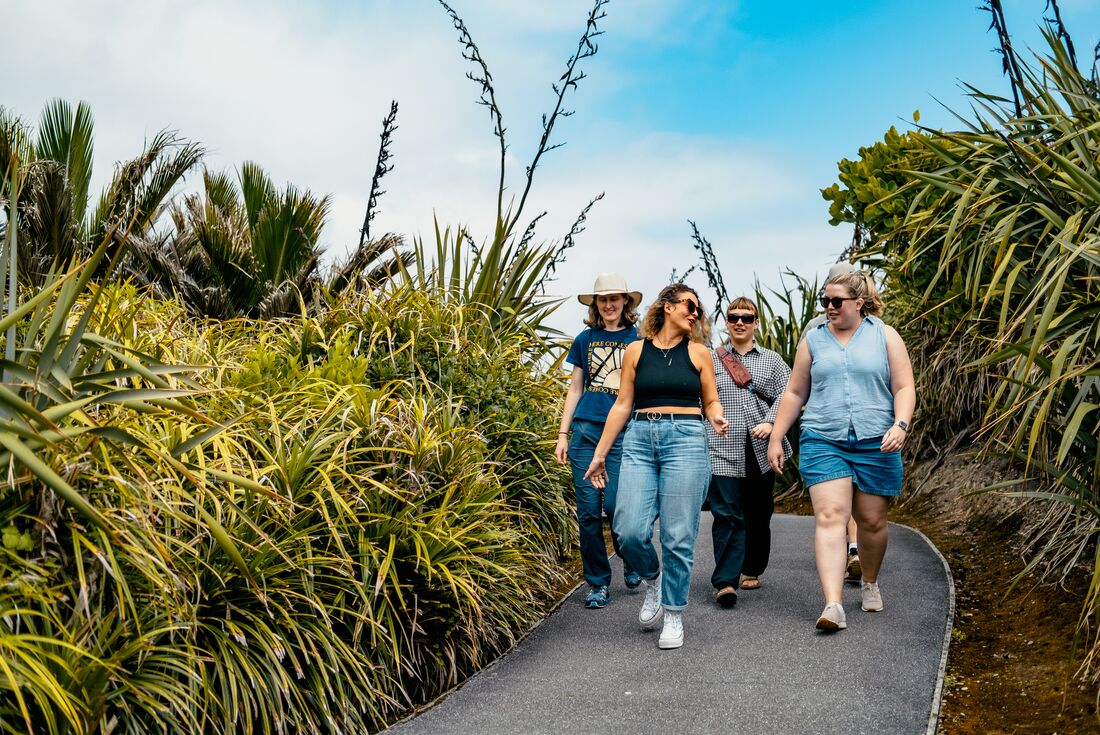 Group of smiling travellers walking on path surrounded by greenery in Punakaiki, New Zealand