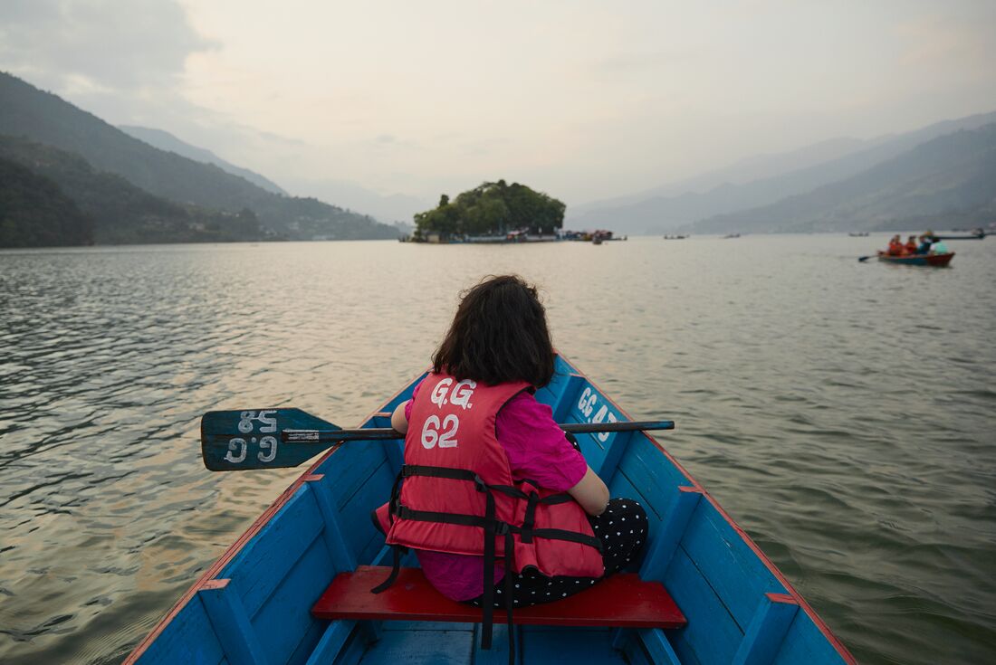 Traveller in lifejacket with paddle on a colourful rowboat on Pokhara Lake in Nepal