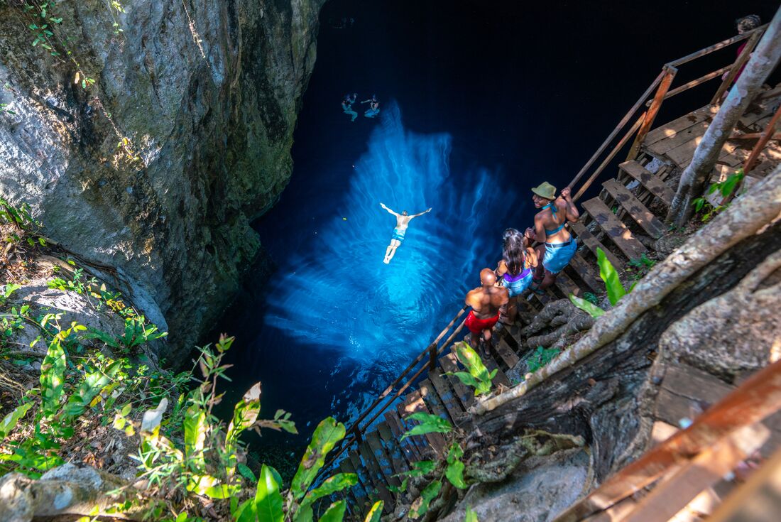 Intrepid travellers watch another swimmer in the reflective crystal blue waters of one of Mexico's cenotes
