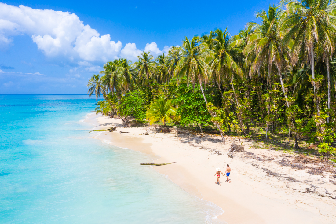 Bocas del Toro beach seen from a drone view with two travellers in swimwear walking down the beach
