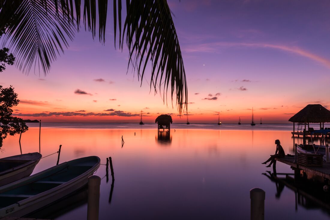 Sunset over the ocean in Caye Caulker Belize with traveller perched on the end of a dock