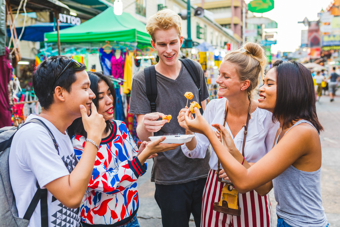 Group of friendly 18 to 35 travellers gather to try some street food balls in Bangkok