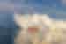 Small orange and white ship Disko Bay ferry overshadowed by huge iceberg in Disko Bay Greenland