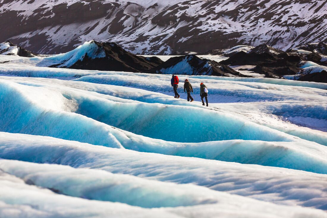 Travellers glacier hiking in Solheimajokull, Iceland with snow covered mountains in the background