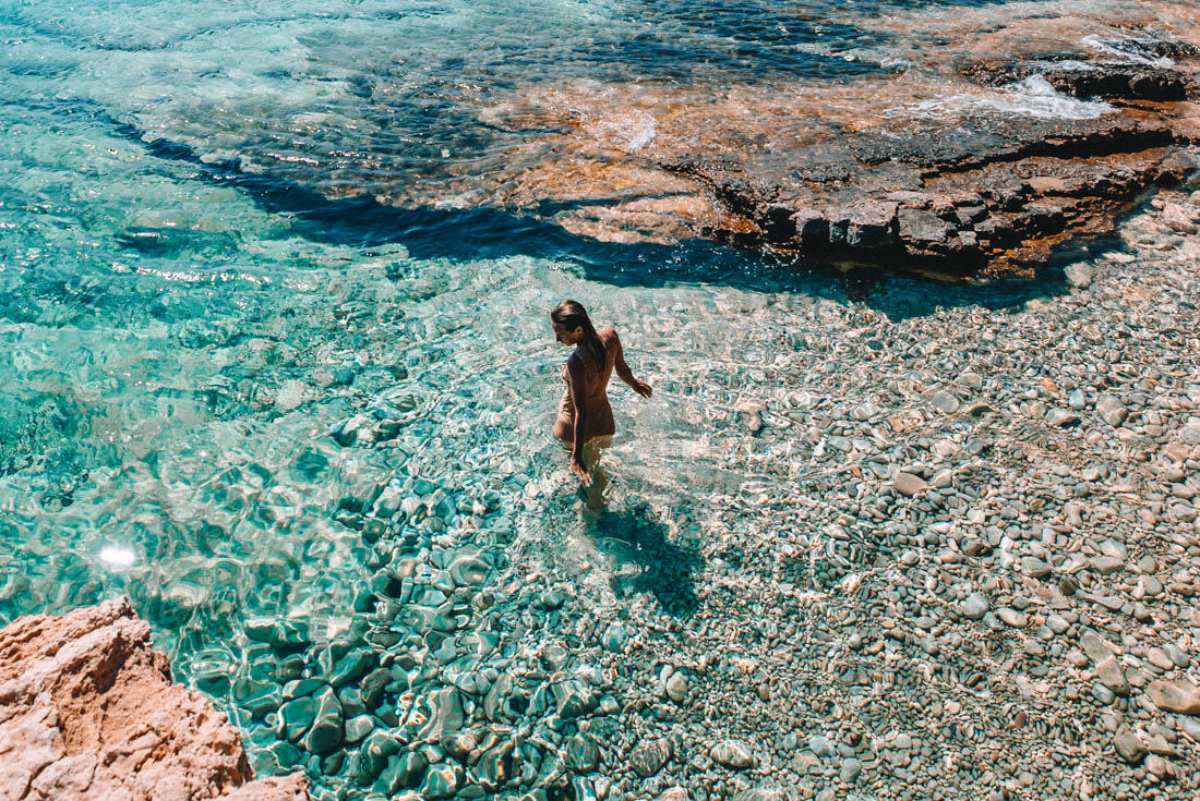 Traveller in swimsuit walks into crystal clear waters of the small Cyclades in Greece