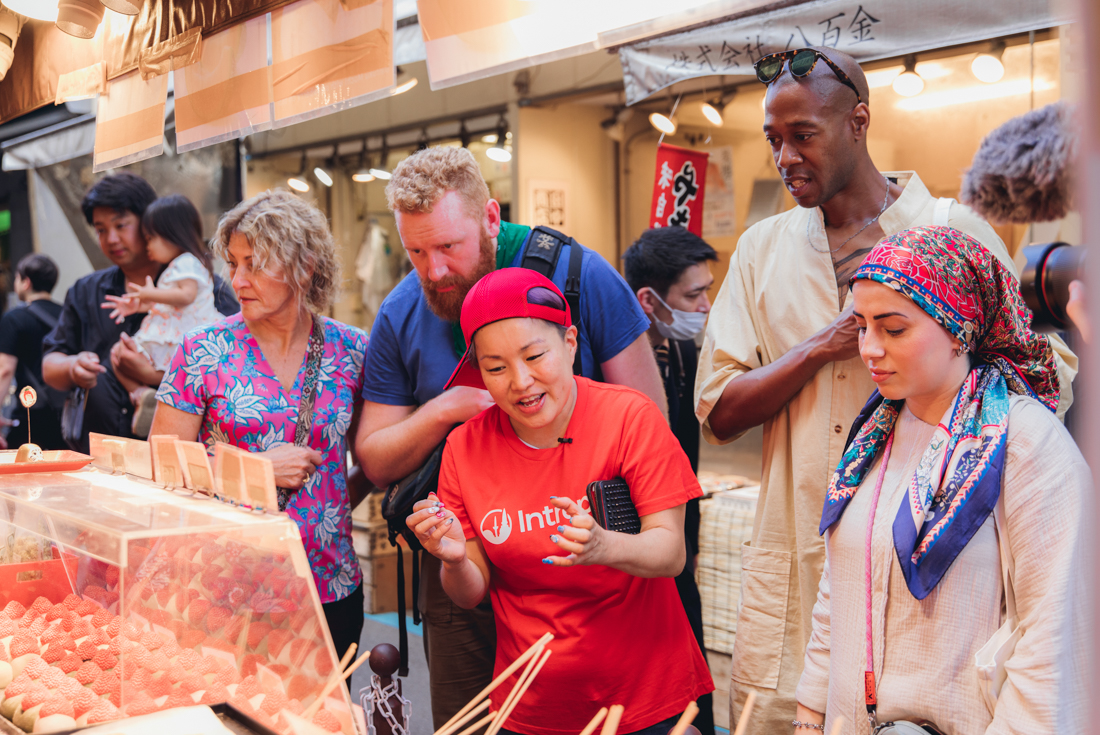 Intrepid travellers and leader look down at desserts in a food market in Tokyo