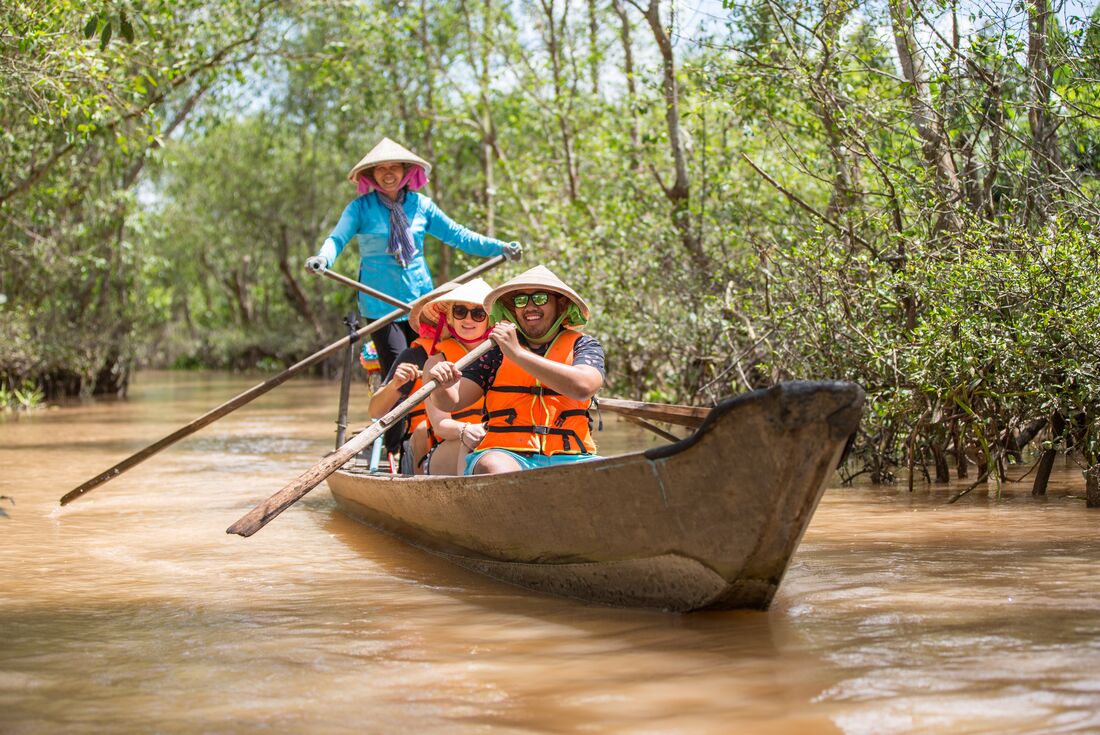 Travellers row along with the smiling guide of the boat tour in the Mekong Delta