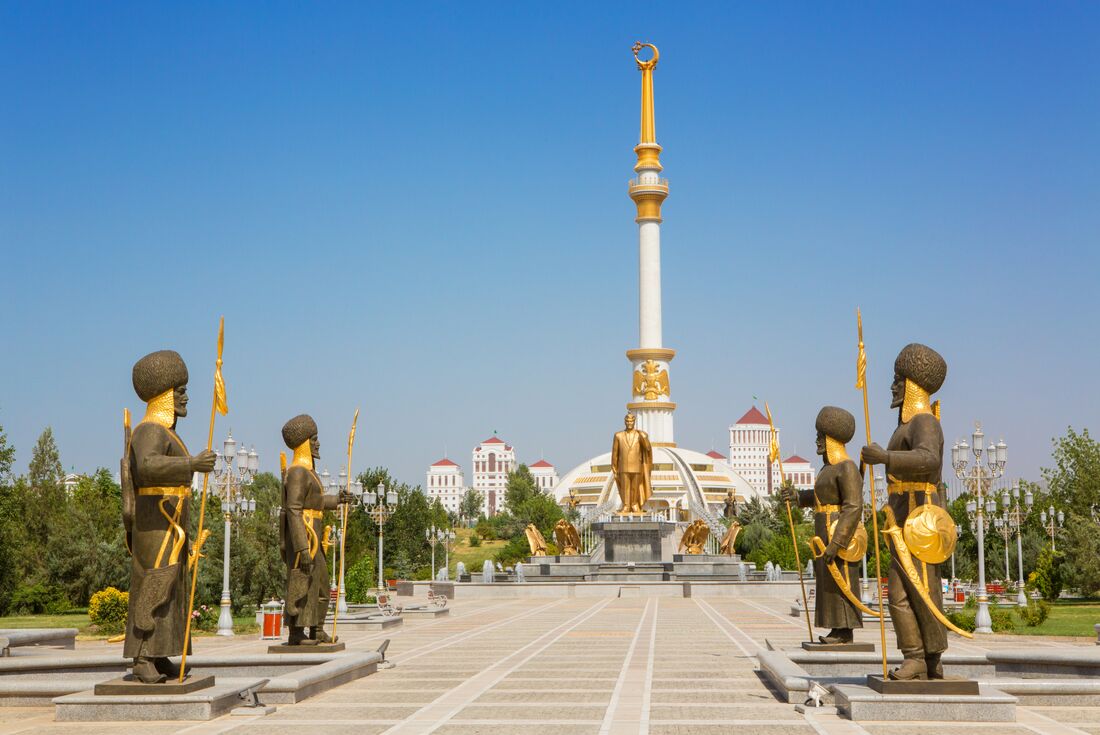 Ashgabat's white marble Independence monument towers over curated forests against a mountain backdrop