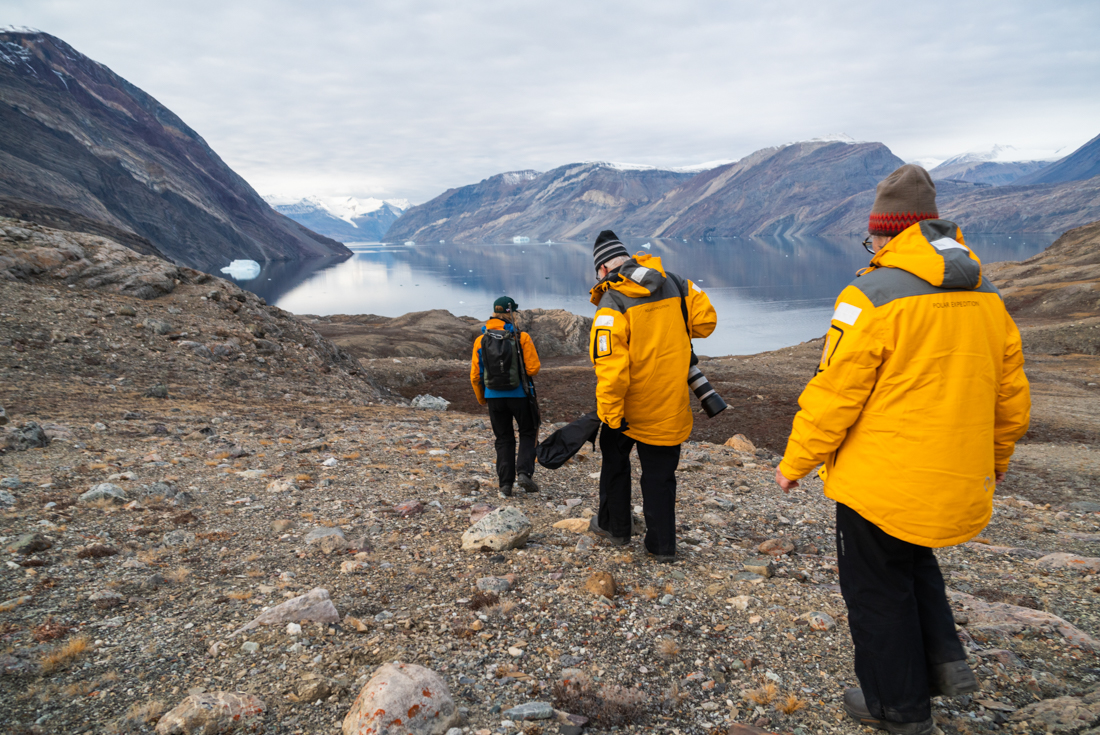 Travellers in yellow Quark coats hiking in the majestic landscape of Blomsterbugten (Flower Bay)