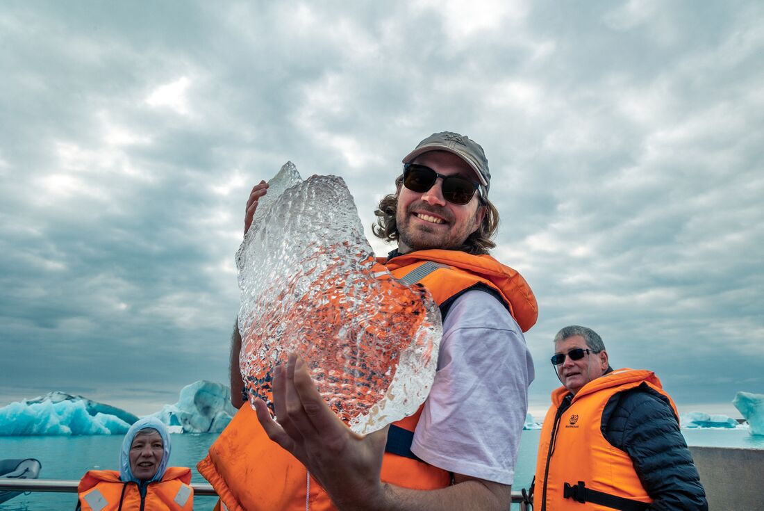 Intrepid traveller smiles, holding a huge shard of fesh ice from the Jokulsarlon Glacier Lagoon in their hands
