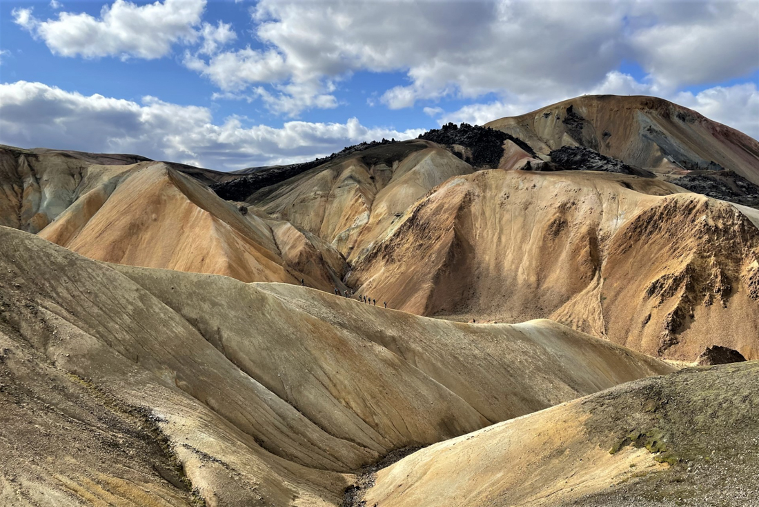 Intrepid travellers hike down a long volcanic soil ridge in the landscape of Iceland
