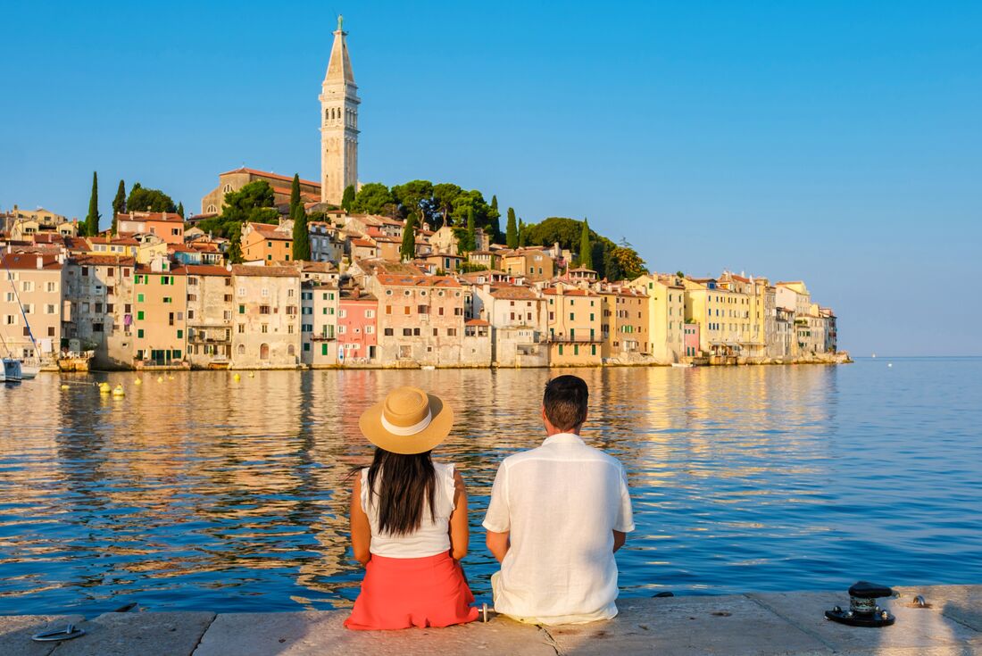 Two travellers sit with their feet in the Adriatic looking out at the waterfront town of Rovinj, Croatia