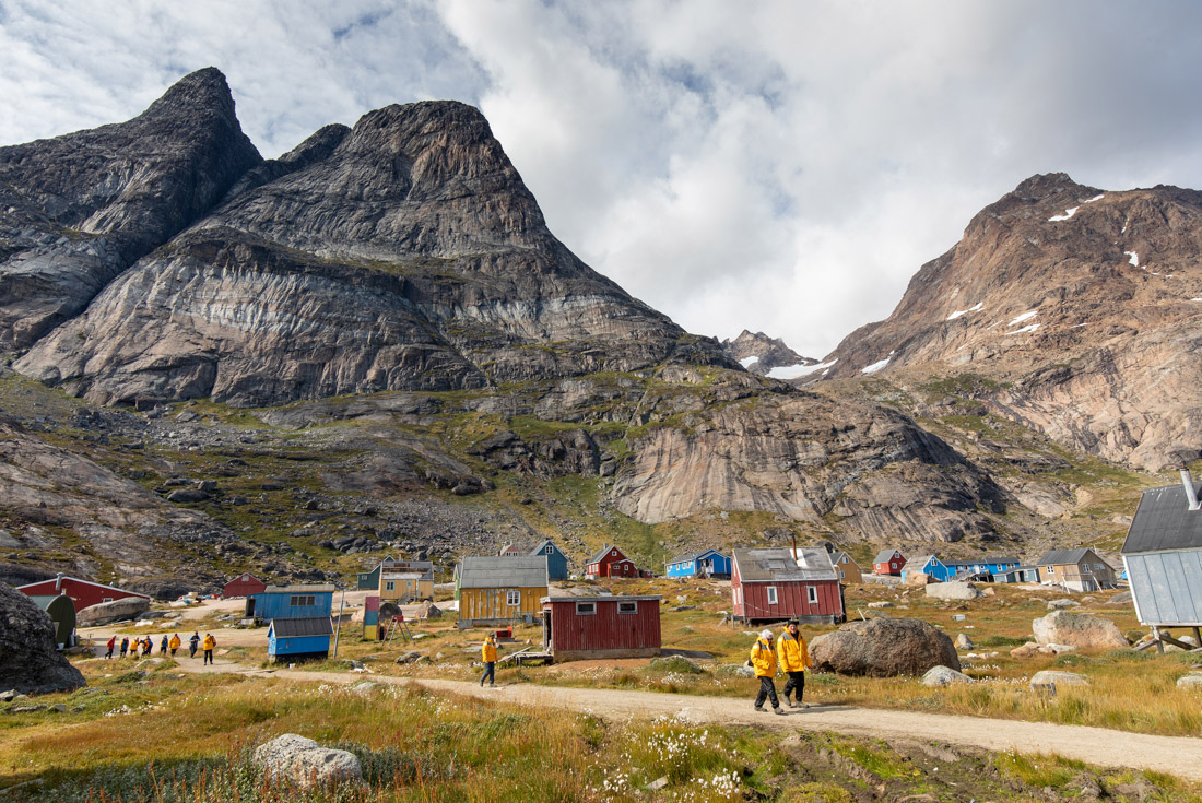 Travellers exploring the town of Aappilattoq in southwestern Greenland with looming mountains