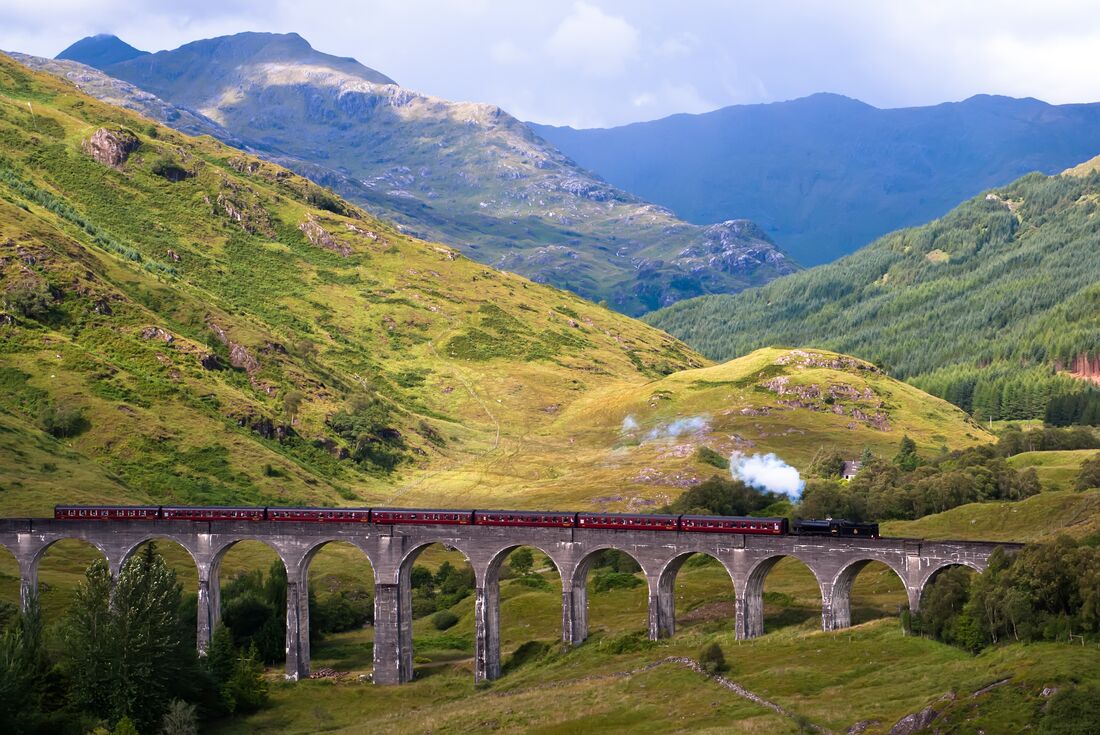 Steam locomotive train crossing an aqueduct bridge with the Scottish Highlands sprawling behind
