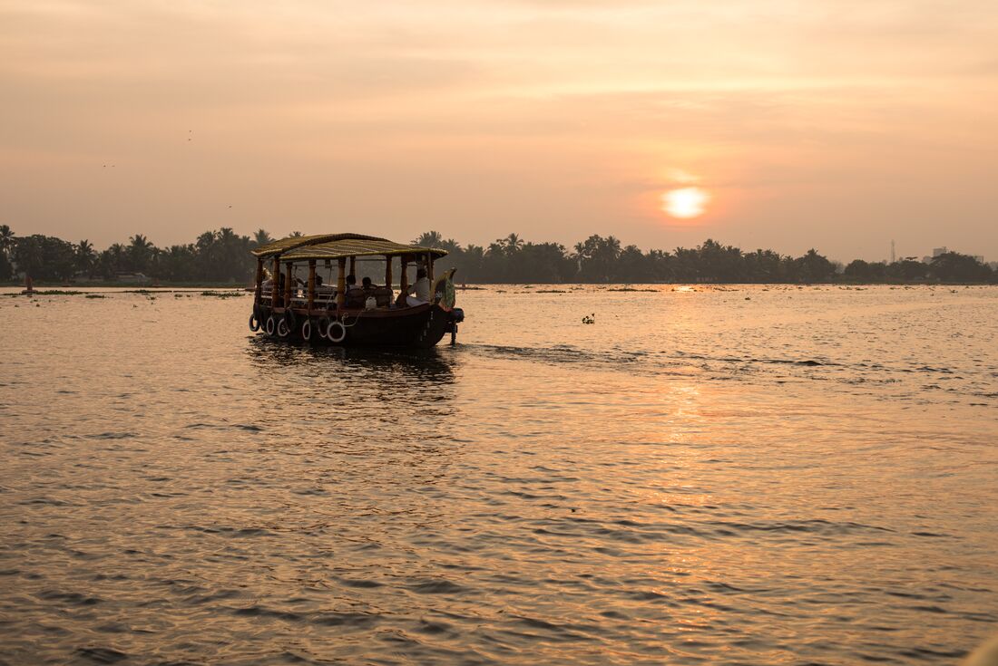 Small cruise ship sails across a lake in the Kerala Backwaters with a red orange sunset in the background