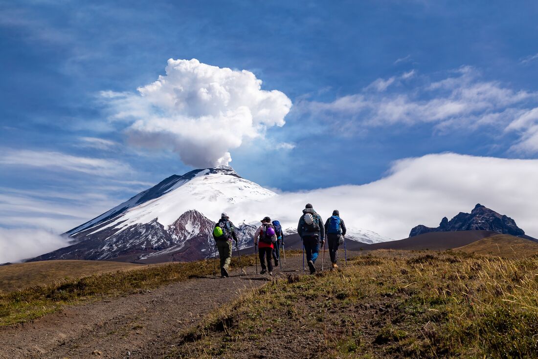 Cotopaxi volcano eruption with travellers hiking in foreground, Cotopaxi NP, Ecuador