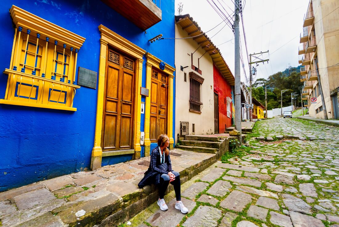 Travelling sitting on the street paved with cobblestone, surrounded by bright colourful buildings in Bogota, Colombia