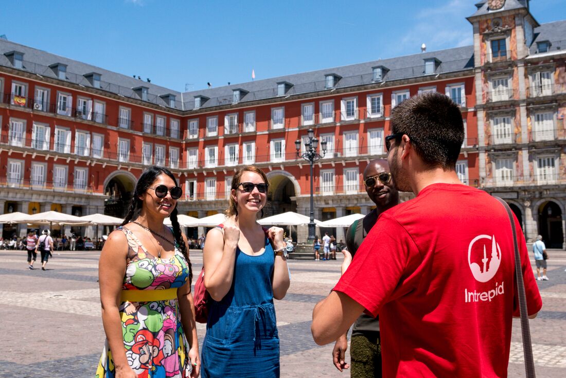 Travellers 18 to 35 with happy faces laugh and smile as leader gives a short talk in the Plaza Mayor in Madrid