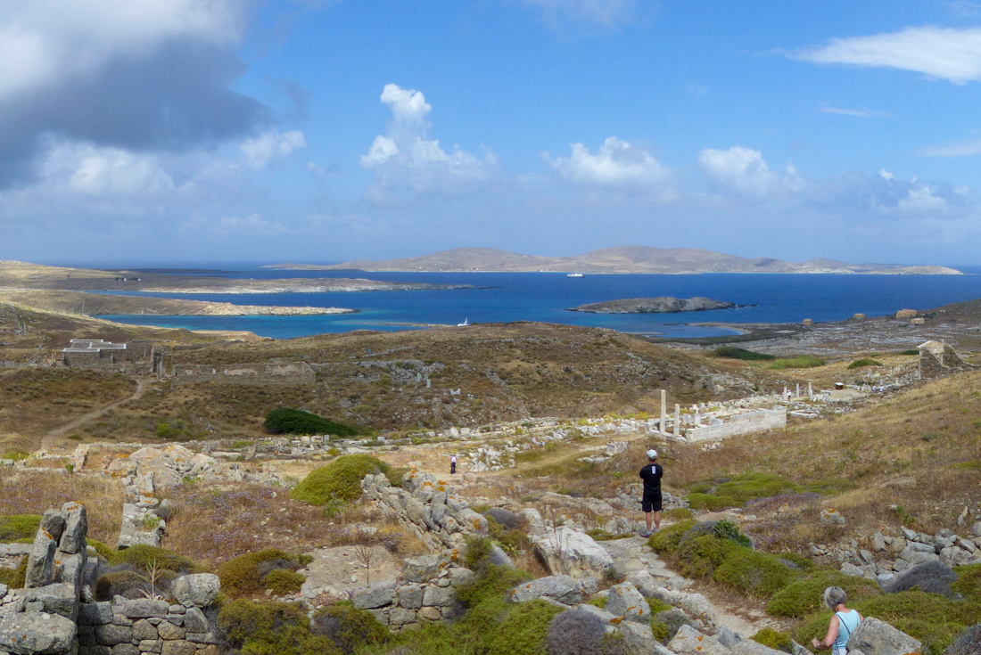 Intrepid traveller at the peak of a hike looking out over Delos and its ruins in the Cyclades