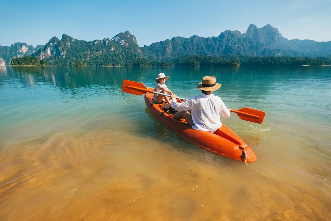 Mother and son push from shore to go kayaking on Cheow Lan Lake in Khao Sok National Park in summer