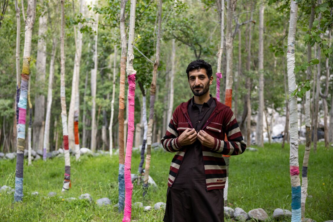 Local from Yugo village stands in front of birch trees with knitted covers to keep goats from eating bark